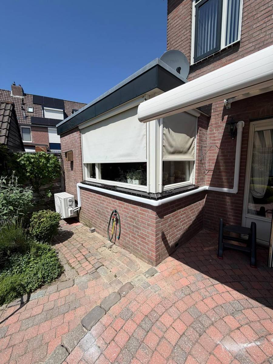 Buitendeel van een airco aan de achtergevel van een woning, leidingen netjes in witte goot